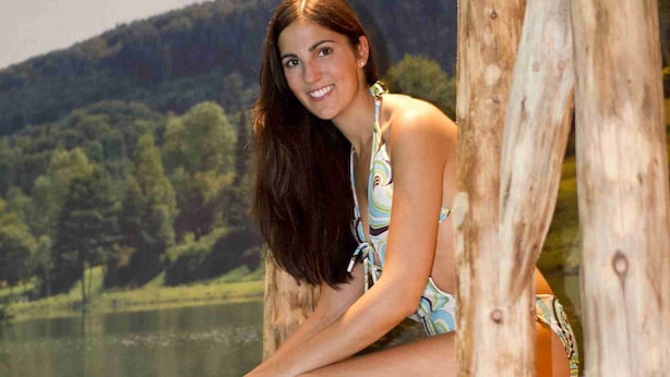 A woman sitting by a wooden pool with a scenic landscape in the background.