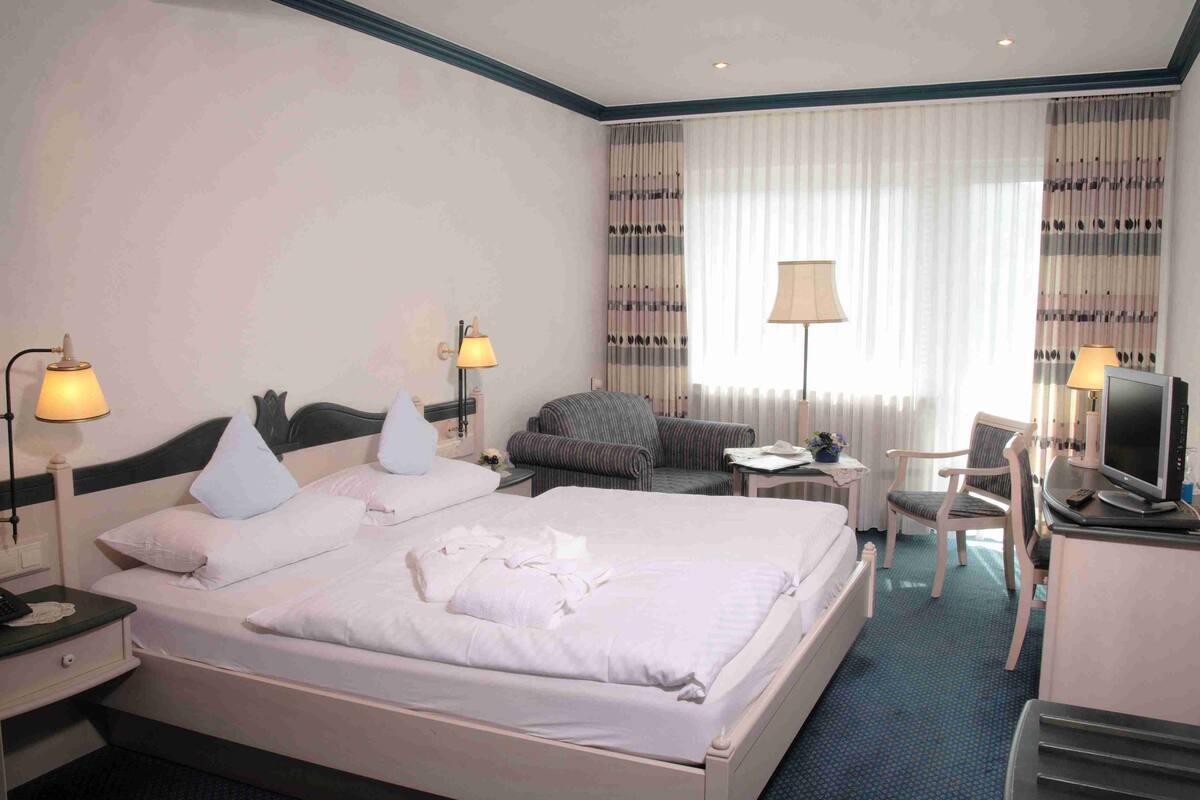 A hotel room with a large bed, two bedside tables with lamps, a small sofa, a desk with a chair, and a television.