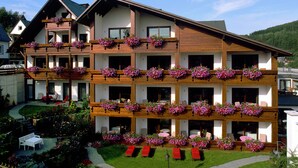 A multi-story hotel with balconies adorned with flower boxes, outdoor seating, and a well-maintained garden.