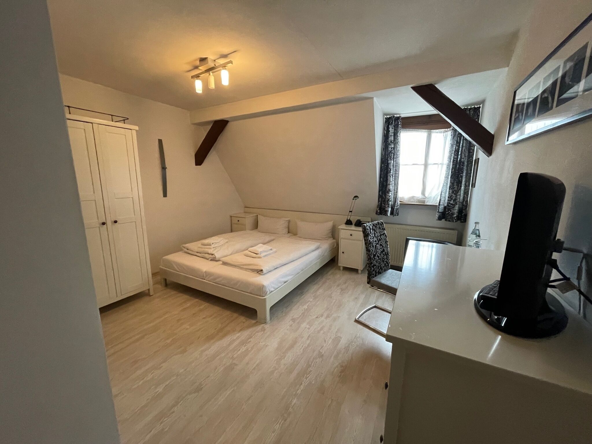 Een slaapkamer met een bed, nachtkastjes, een bureau, een stoel, een kledingkast en een plafondlamp.