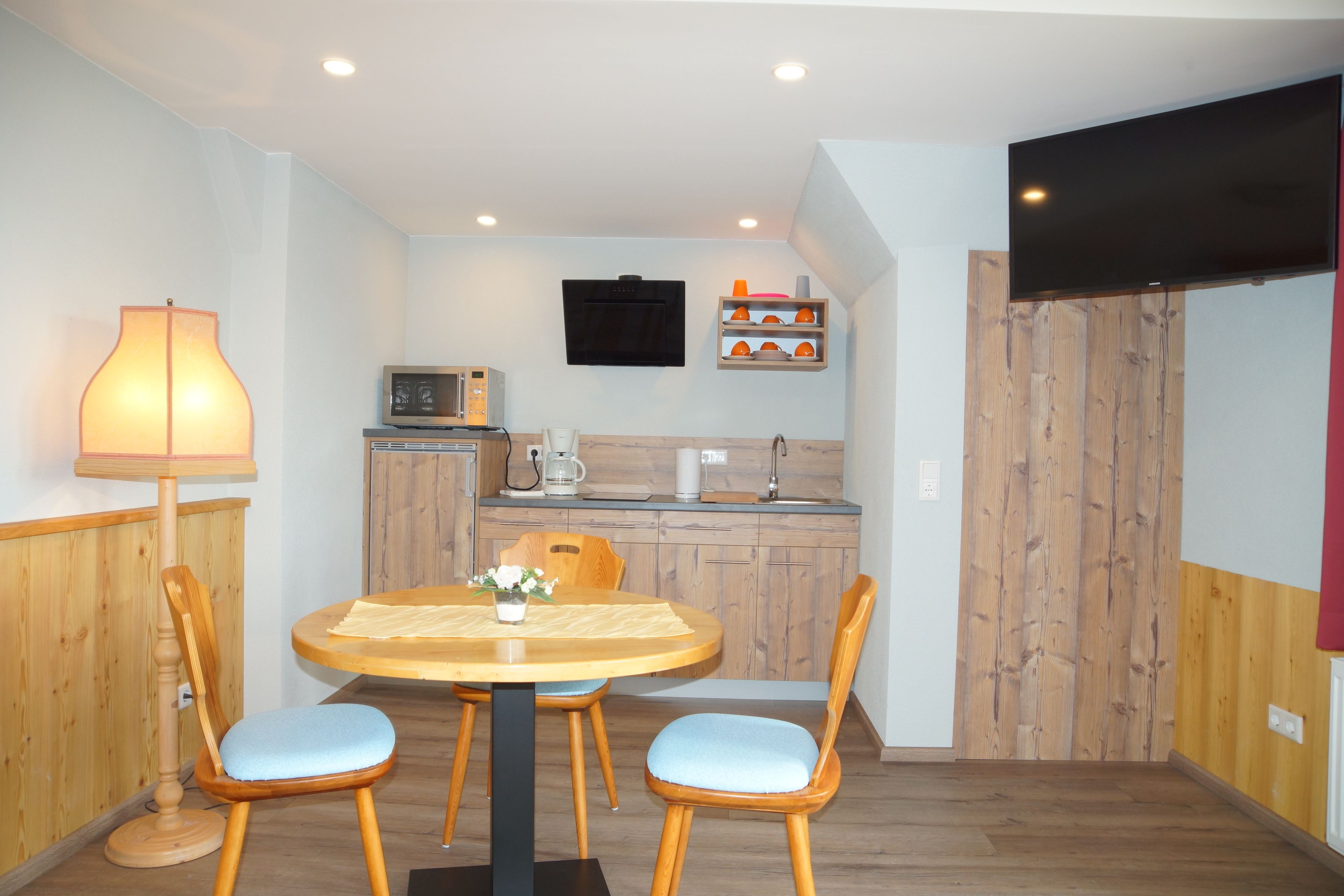A compact kitchen with a microwave, coffee maker, and a flat-screen TV mounted on the wall.