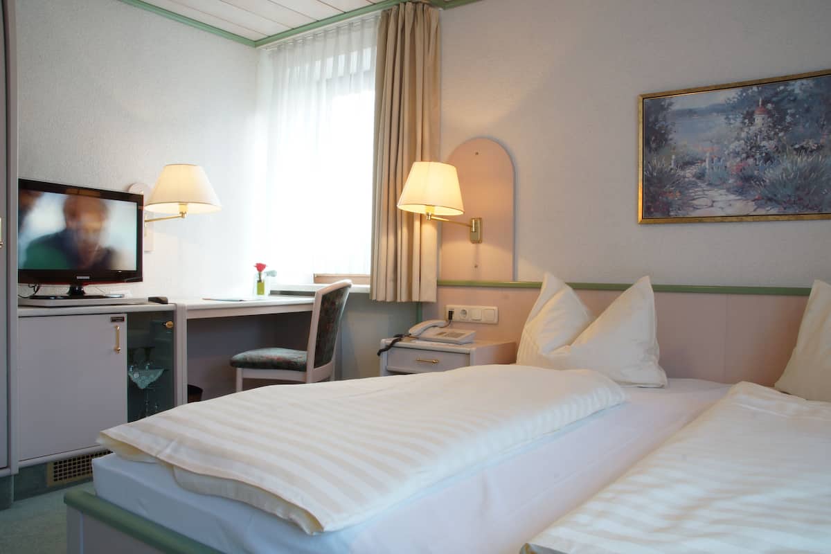 A hotel room with a bed, a desk with a computer, a TV, and a painting on the wall.