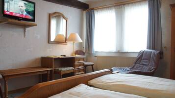 Habitación de hotel con cama, escritorio con silla, lámpara, espejo y televisor en la pared.