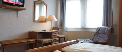 A hotel room with a bed, a desk with a chair, a lamp, a mirror, and a television on the wall.