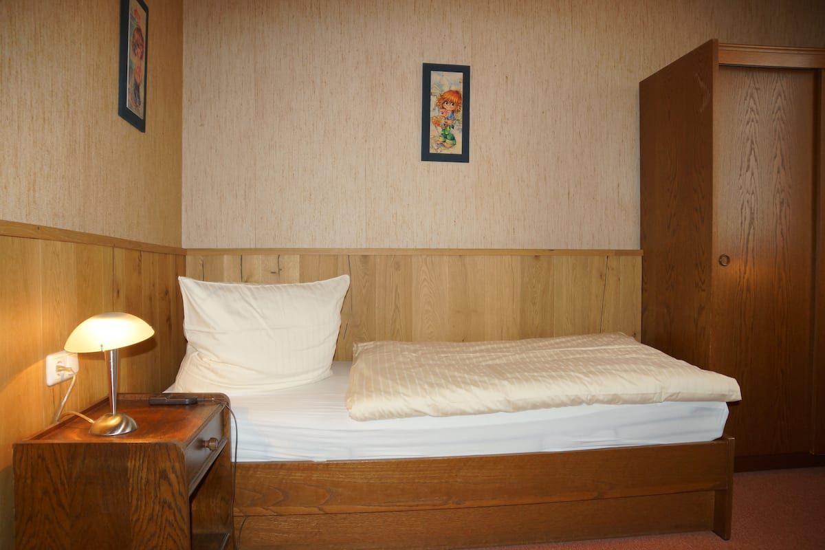 A wooden bed with white bedding, a nightstand with a lamp, and a wooden wardrobe.
