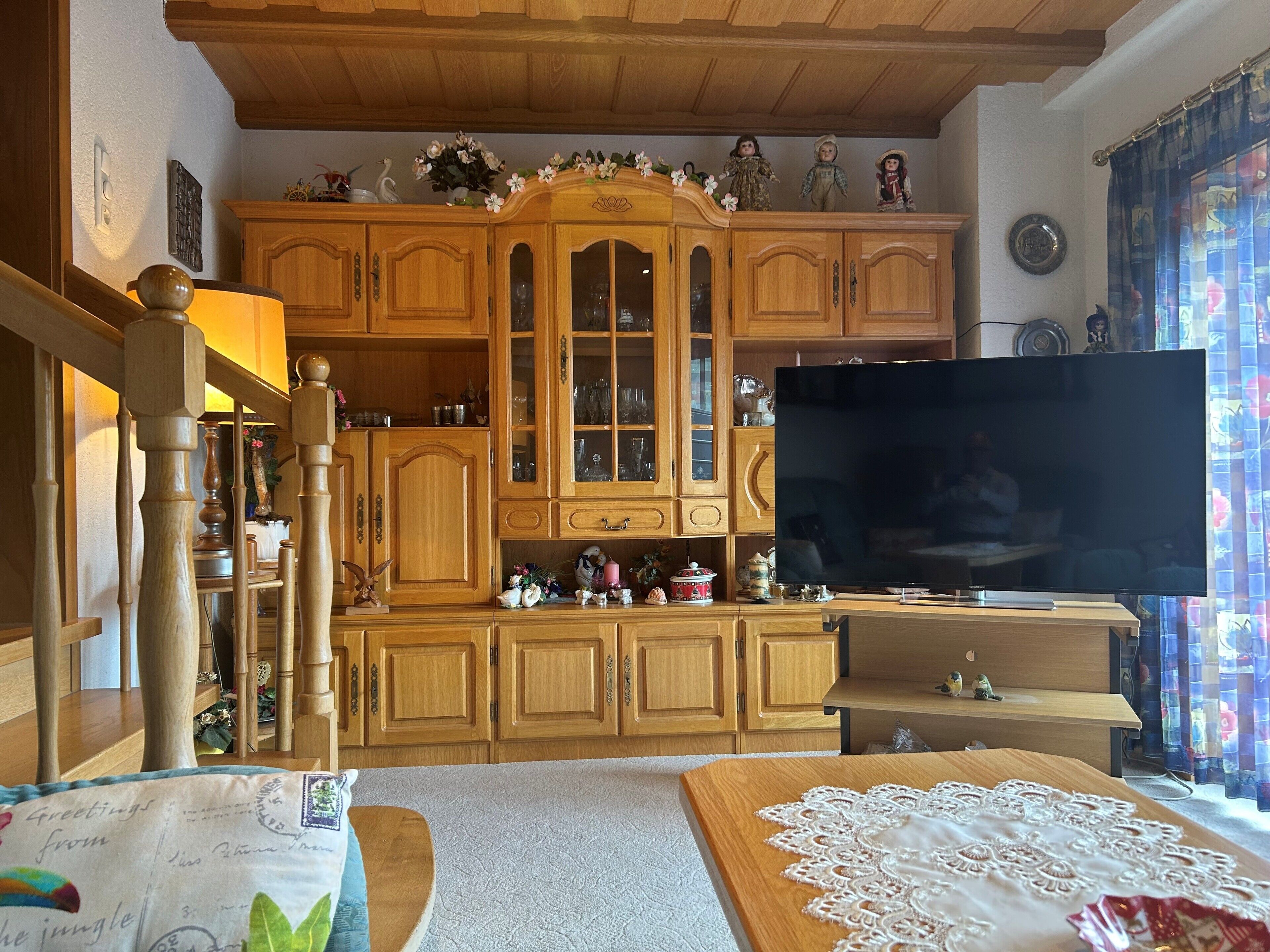 Un mueble tradicional de madera con puertas de cristal, un televisor de pantalla plana y un encaje decorativo sobre una mesa.