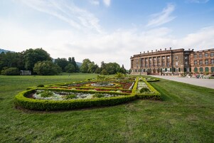 A formal garden with geometric flower beds and a large building with classical architecture in the background.