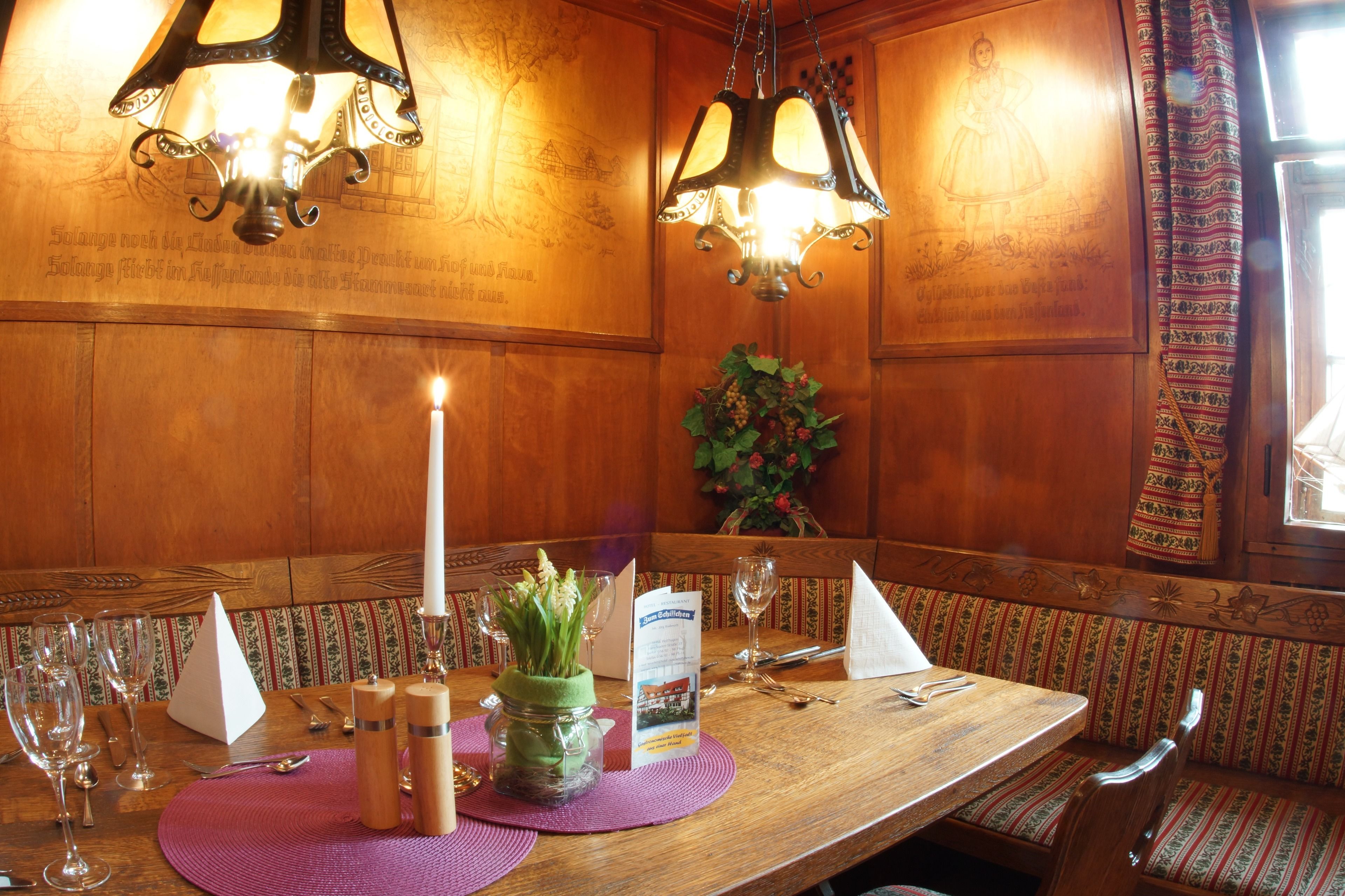 Una mesa de madera para comer con una vela, copas de vino y un menú.