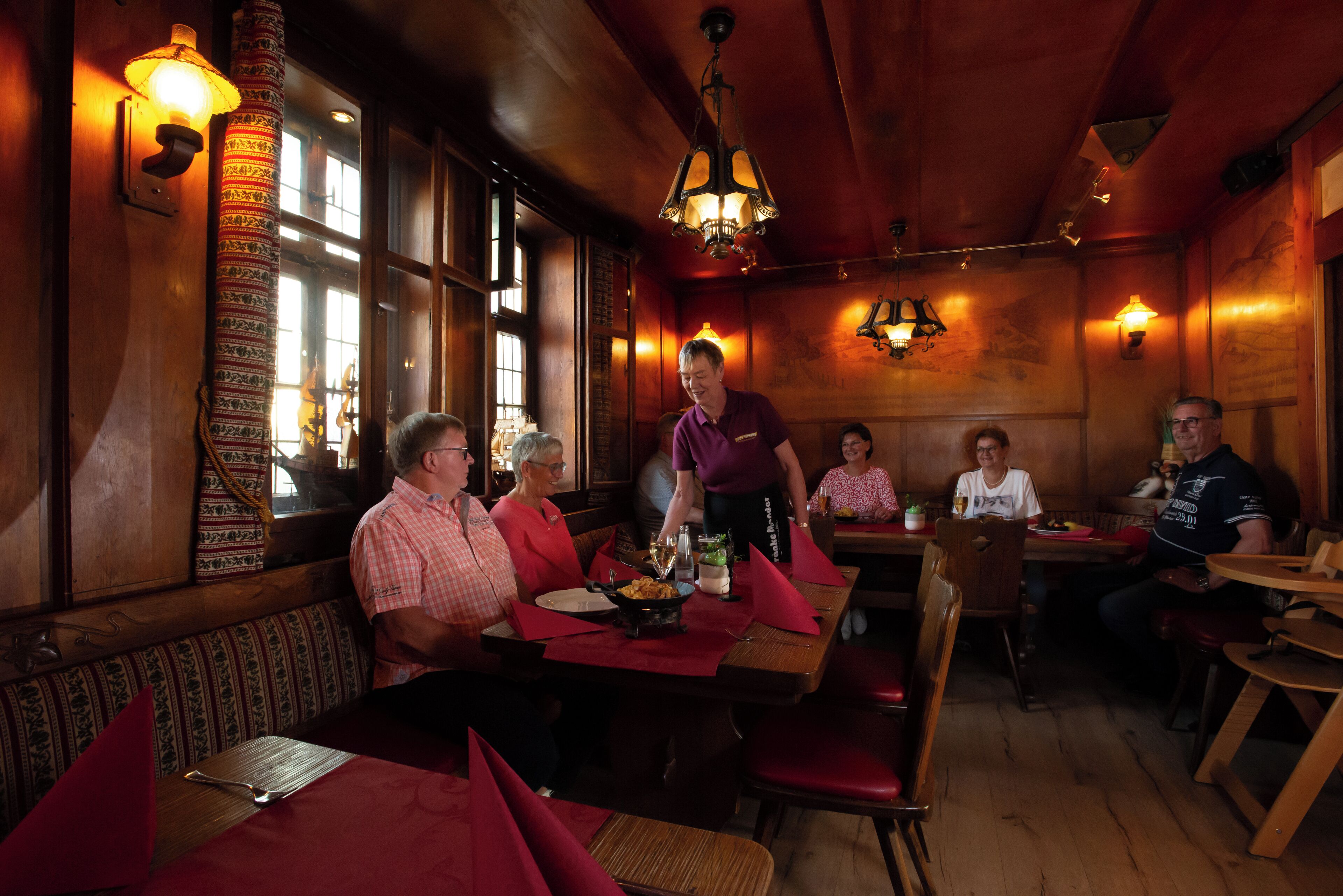 Restaurante com paredes de madeira, colunas com padrão e assentos acolchoados vermelhos.