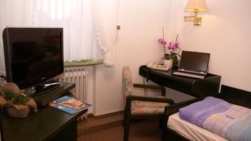 A small, neatly arranged room with a bed, a desk with a laptop, a chair, a television, and a lamp.