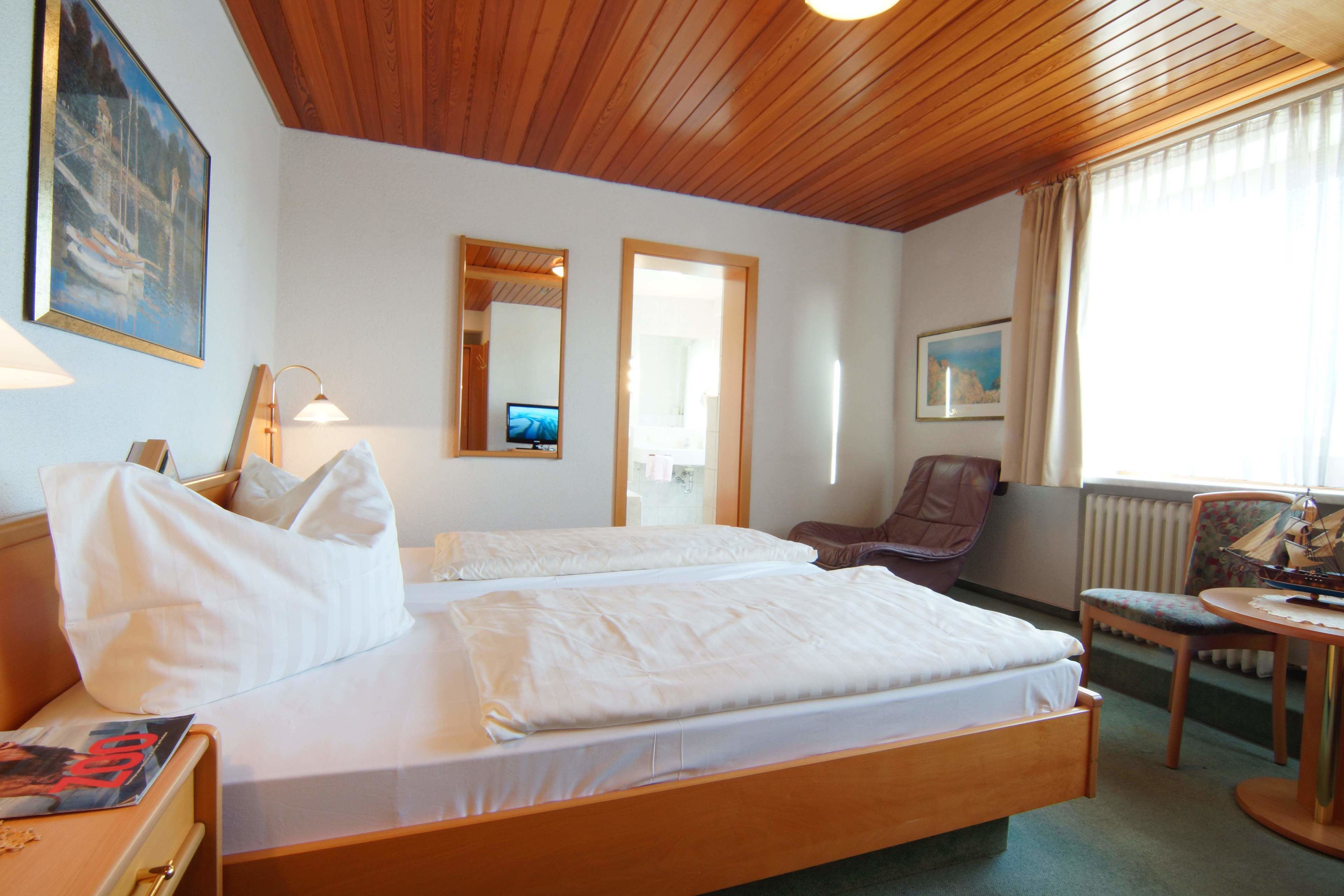 A hotel room with a wooden ceiling, two beds with white bedding, a desk with a chair, a television, and a window with curtains.