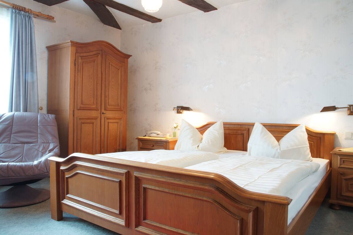 A bedroom with a wooden bed, nightstands, a wardrobe, and a chair.