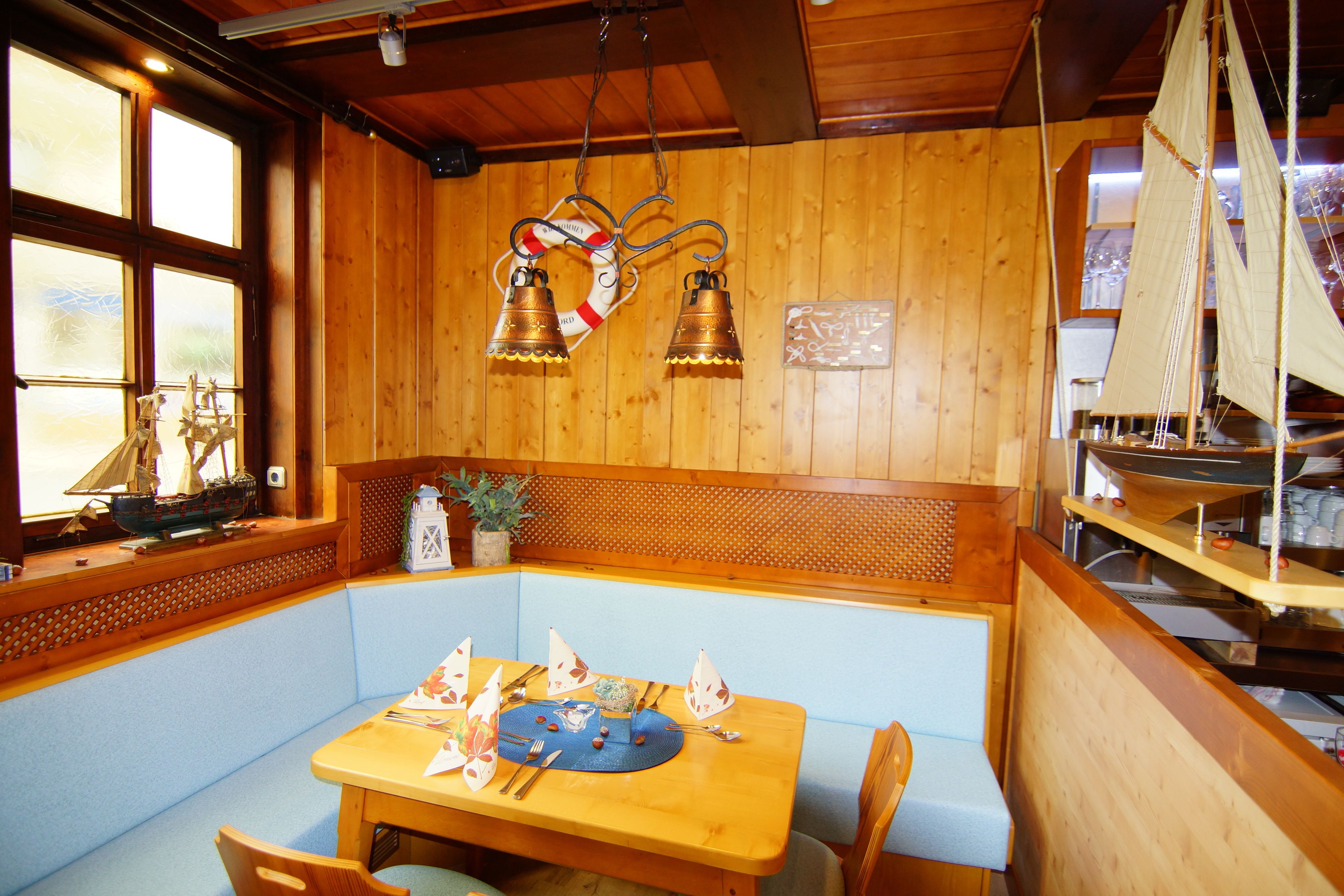 A wooden interior with a table set for dining, a bench, and a decorative sailboat model.
