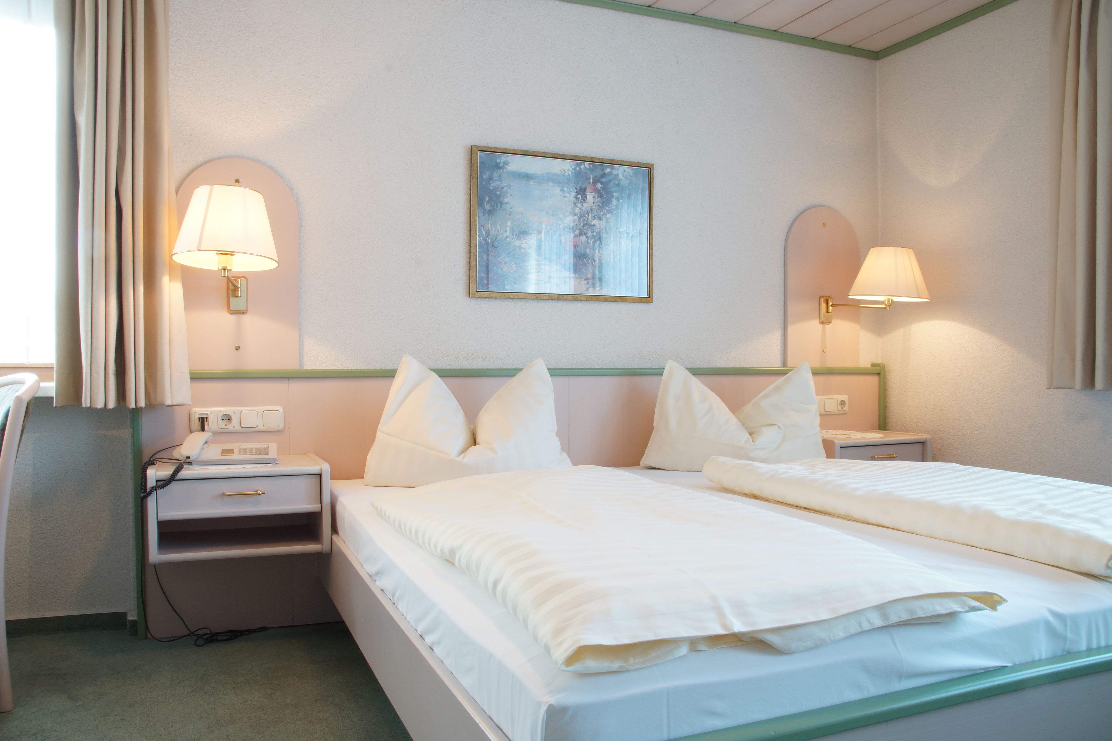Habitación de hotel con dos camas, una mesita de noche, una lámpara, un cuadro en la pared y una ventana con cortinas.