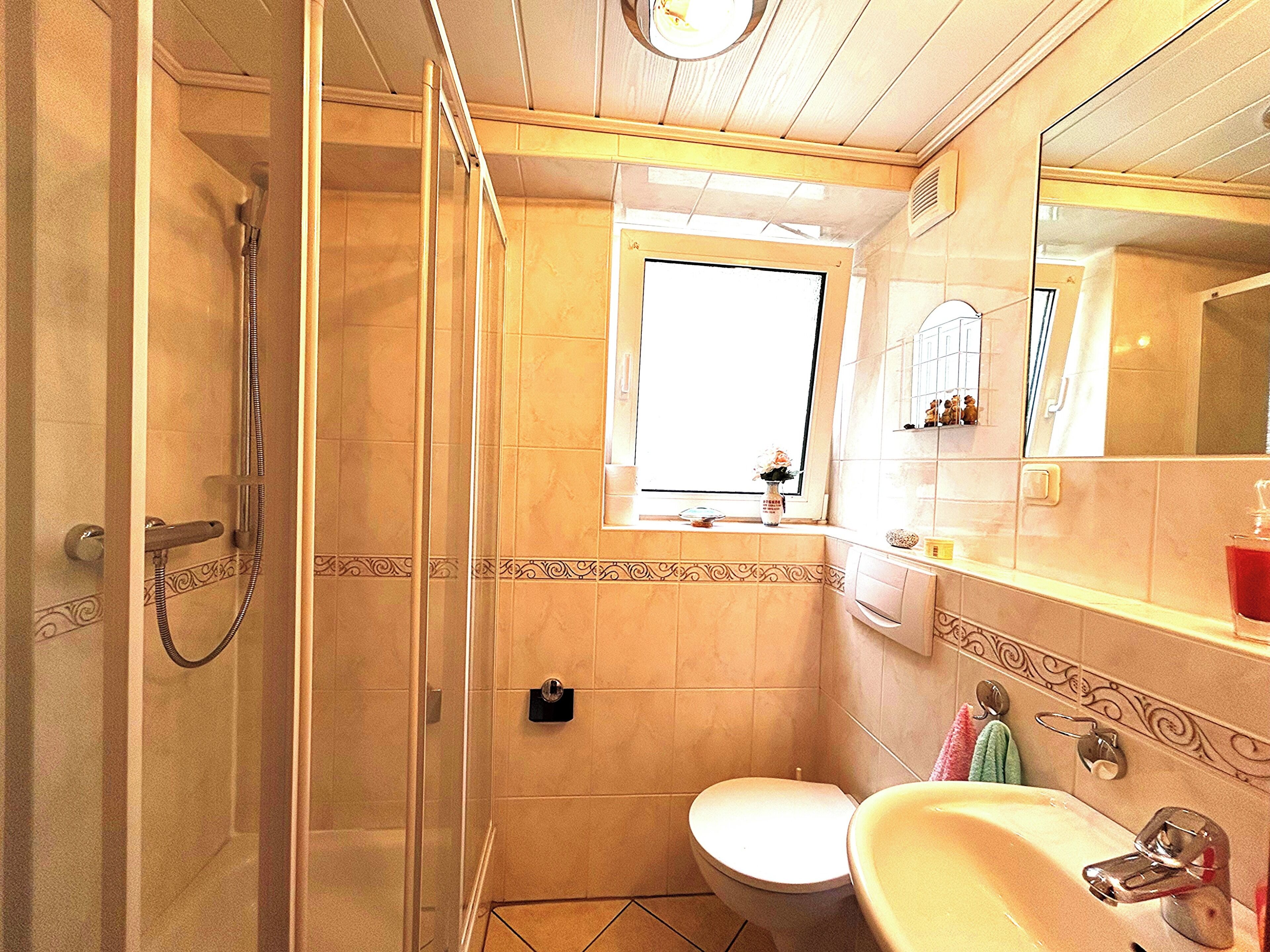 Ein Badezimmer mit Dusche, Toilette, Waschbecken und einem Fenster.
