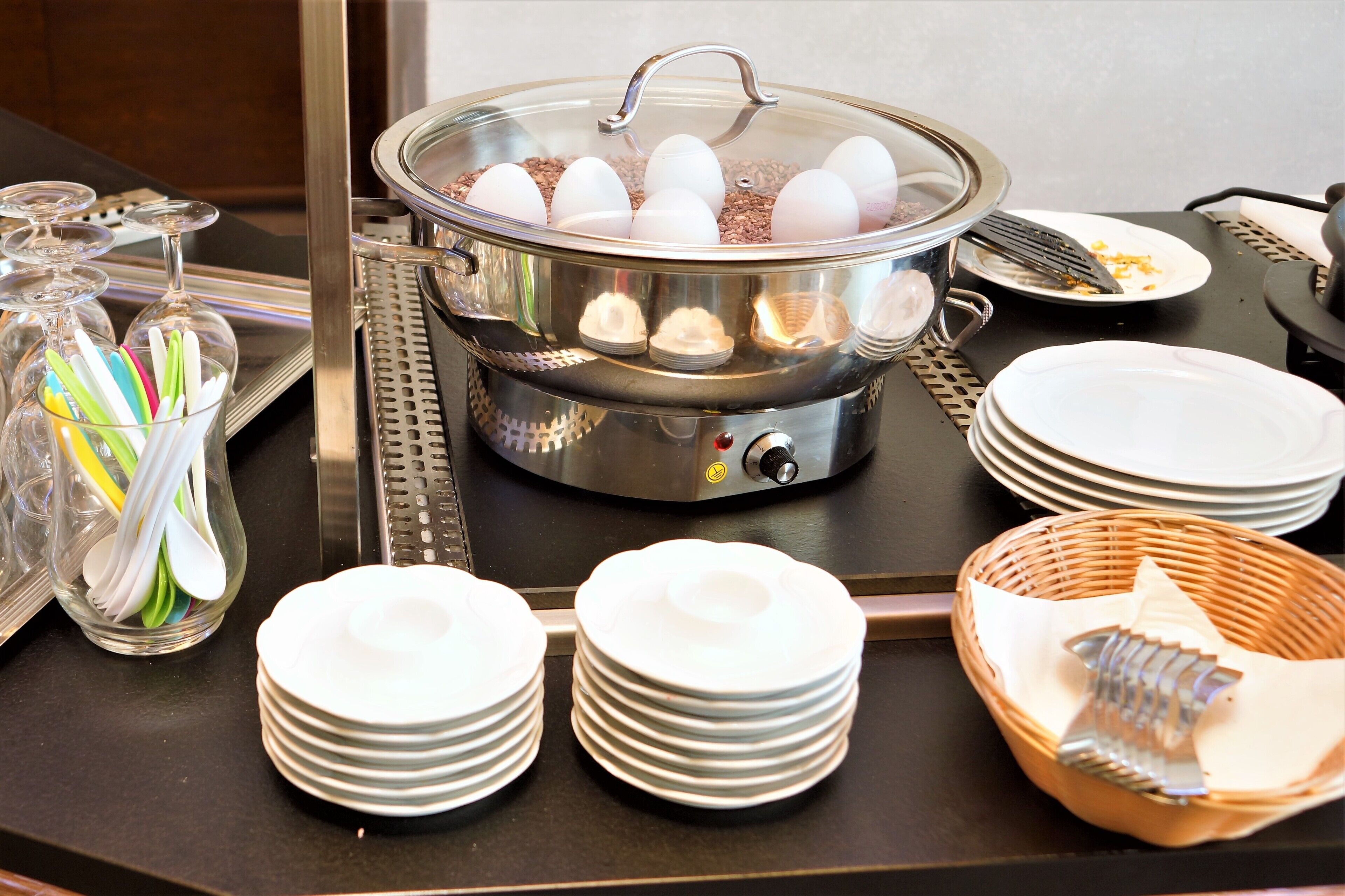 Ein Buffet mit einem Hot Pot, gestapelten weißen Tellern und einer Servierschale für Besteck.