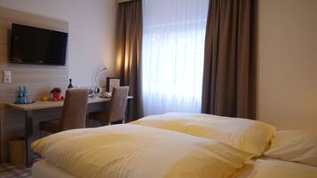 Ein Hotelzimmer mit Bett, Schreibtisch mit Stuhl, Flachbildfernseher und einem Fenster mit Vorhängen.
