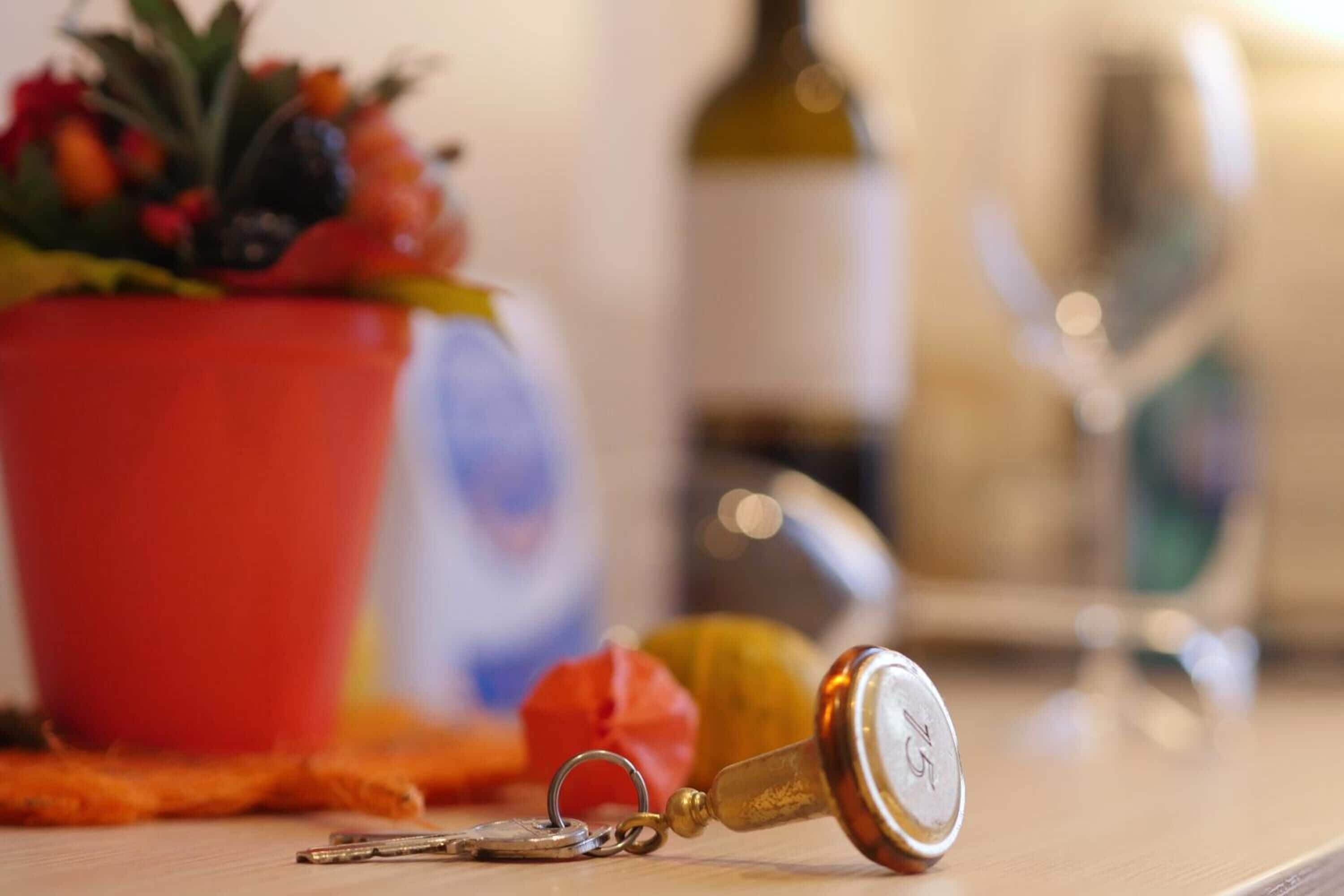 A keychain with a bottle cap, a red pot with flowers, and a blurred bottle in the background.
