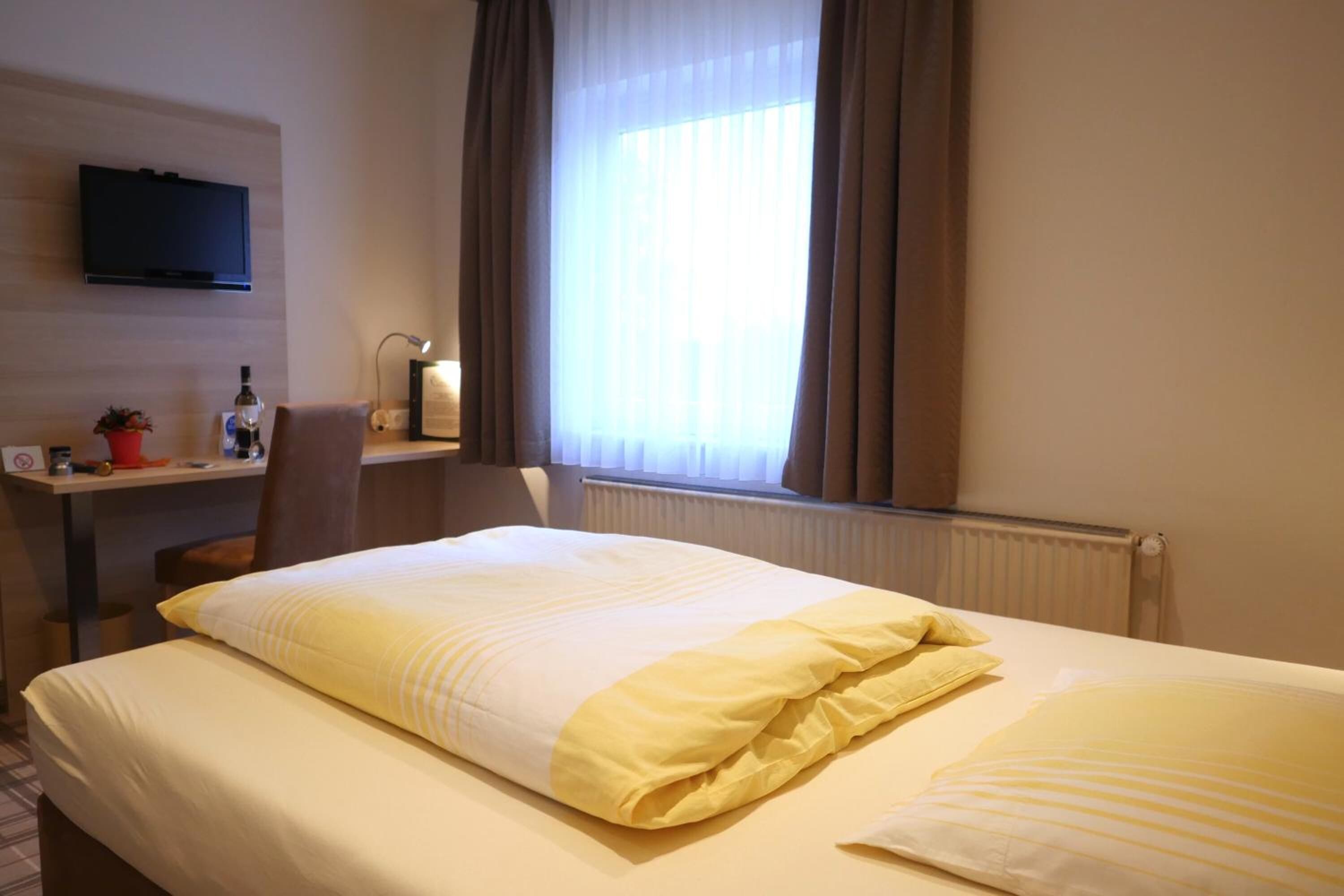 Une chambre d’hôtel équipée d’un lit, d’un bureau, d’une chaise, d’une télévision et d’une fenêtre avec des rideaux.