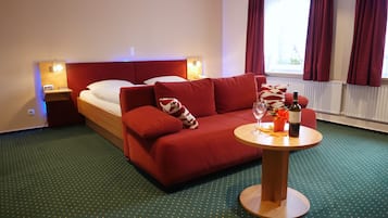 Hotelkamer met een bed, rode bank, kleine tafel met een fles en glazen, en een raam met gordijnen.