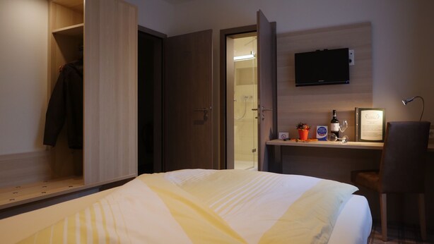 A hotel room with a bed, a desk with a chair, a TV mounted on the wall, and a wardrobe with a mirror. - Gasthof Vossbur (Toppenstedt)