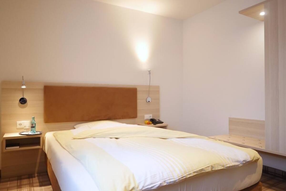 A hotel room with a large bed, a bedside table with a lamp, and a wall-mounted light fixture.