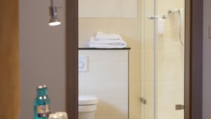 A bathroom with a glass shower enclosure, a toilet, and a sink with a bottle and glasses on the counter. - Gasthof Vossbur (Toppenstedt)