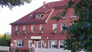 A red brick building with a sign reading "Gasthof Vossbur." It has multiple windows, some with flower boxes, and a white picket fence in front. - Gasthof Vossbur (Toppenstedt)