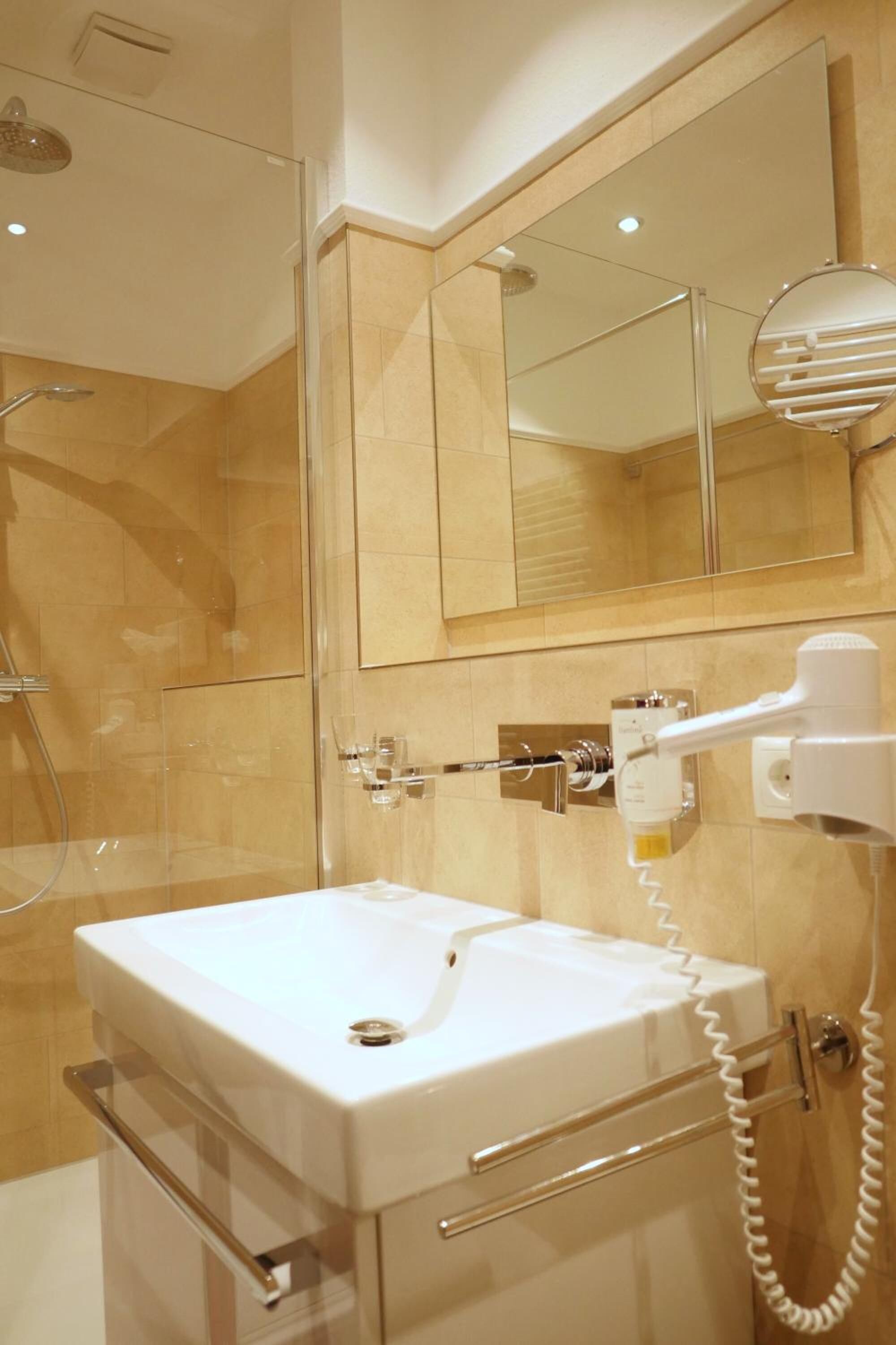 A modern bathroom with a glass shower enclosure, a white sink with a towel rack, and a hairdryer mounted on the wall.