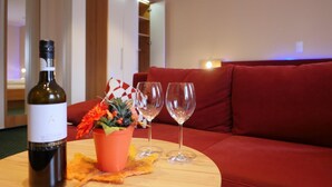 A room with a red sofa, a wooden table with a bottle of wine, two glasses, and a potted plant. - Gasthof Vossbur (Toppenstedt)