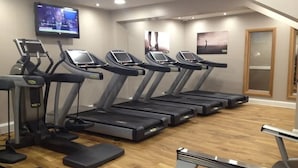 Un gimnasio con cintas de correr y una pantalla de televisión que muestra un noticiero.