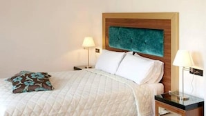 Una cama bien hecha con una cubierta blanca acolchada, dos lámparas de noche y un cabecero de madera con detalles en color aguamarina.