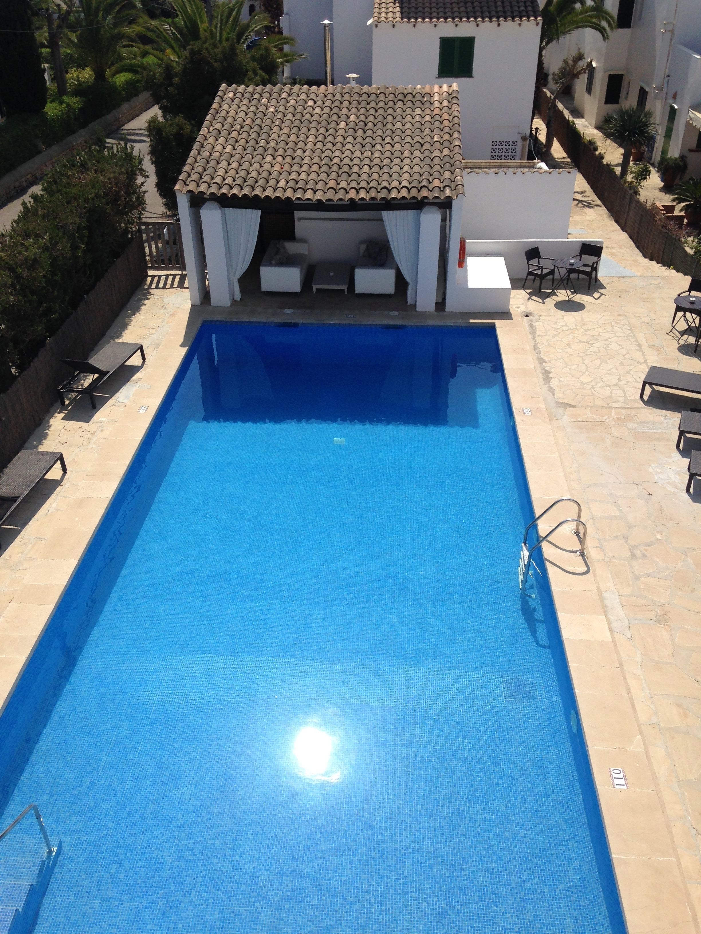 Una piscina rectangular amb una zona enrajolada al voltant. Hi ha gandules i una petita zona d'estar amb una taula i cadires.