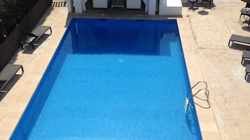 Una piscina rectangular amb una zona enrajolada al voltant. Hi ha gandules i una petita zona d'estar amb una taula i cadires.