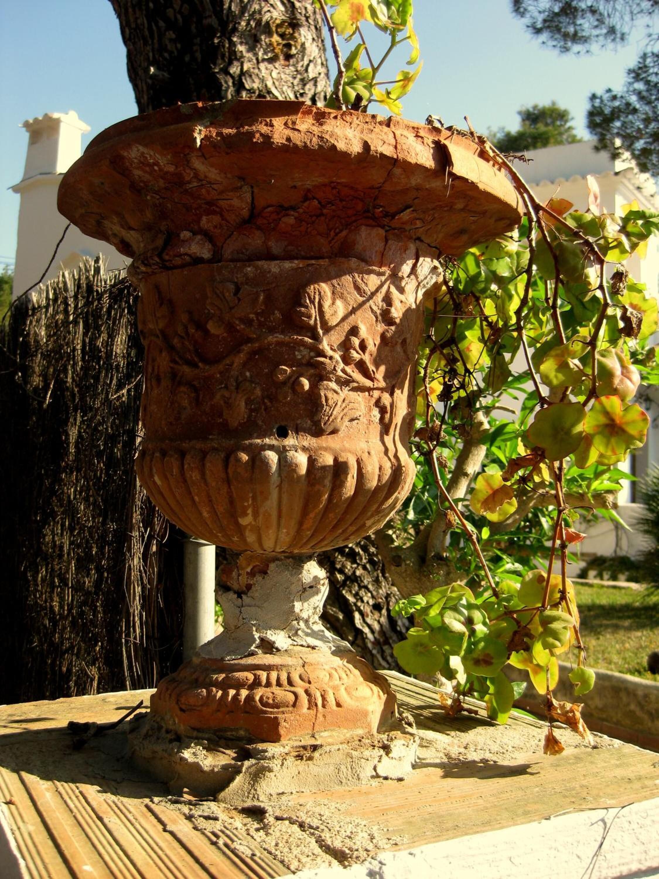 A large, weathered terracotta planter with intricate carvings, placed on a wooden surface outdoors.