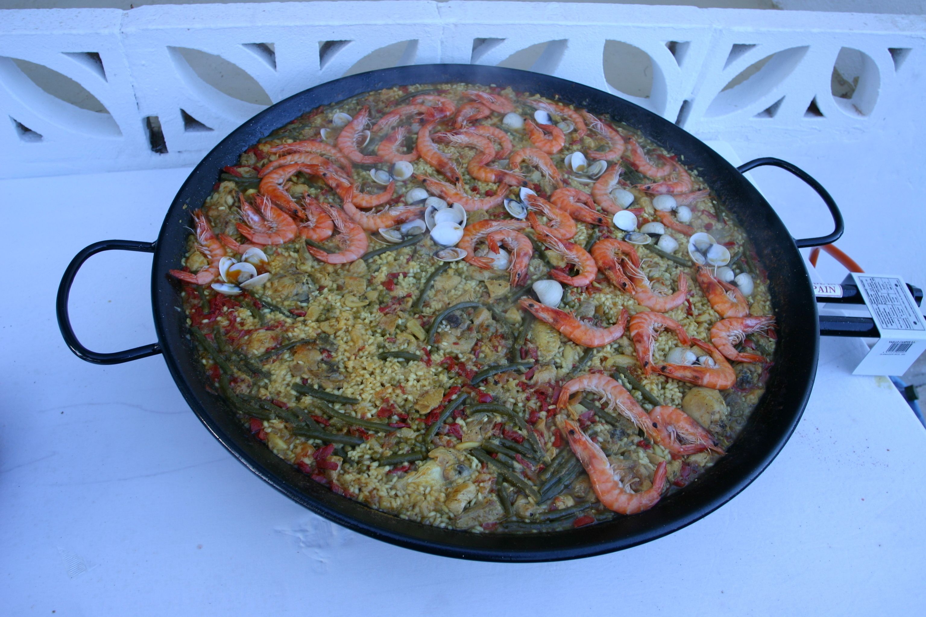 A large black pan filled with seafood paella on a white surface.