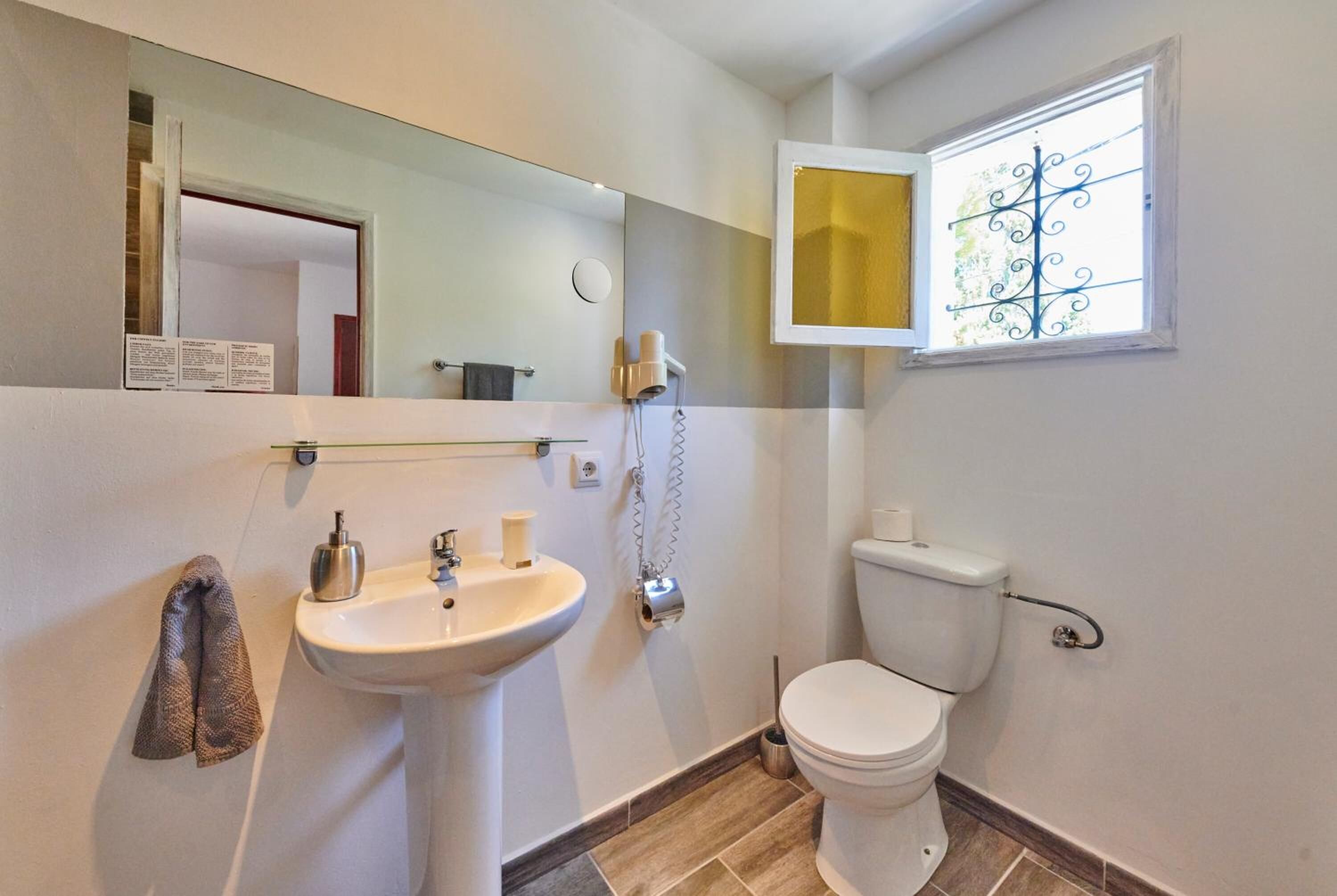 Une petite salle de bain comprenant un lavabo, des toilettes et une fenêtre ornée d’une grille décorative.