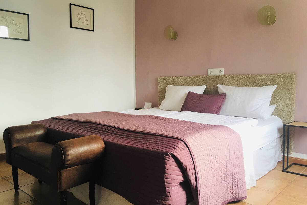 Une chambre bien rangée, avec un lit, une chaise et deux œuvres d’art encadrées accrochées au mur.