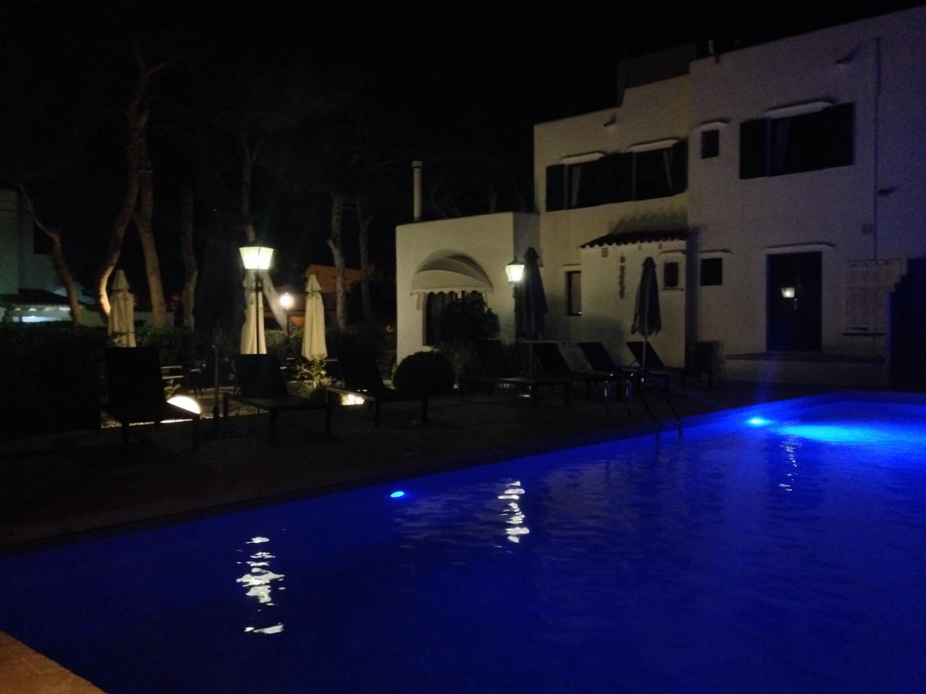 An outdoor swimming pool with blue lighting, lounge chairs, and umbrellas.