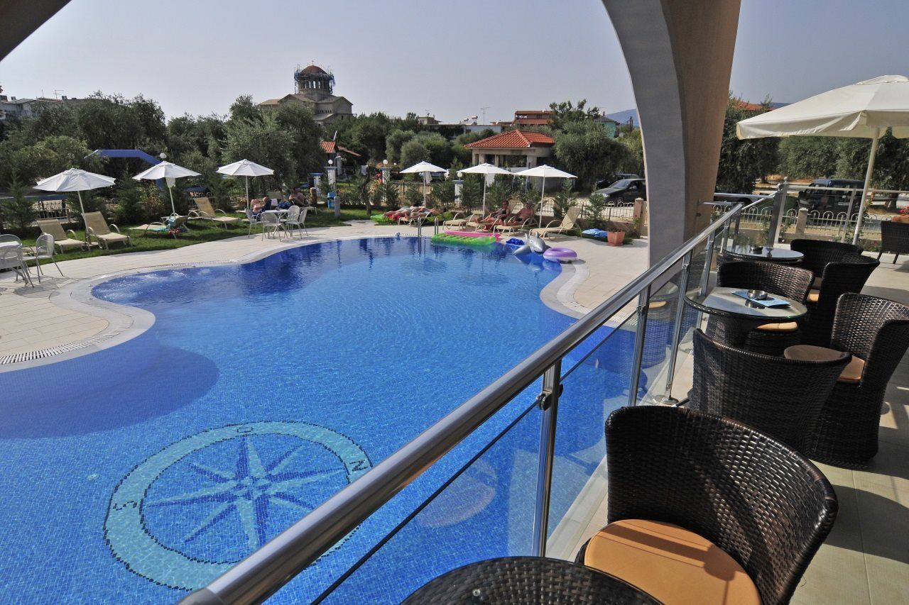 A swimming pool with lounge chairs and umbrellas, a view of a building in the background, and a railing overlooking the pool.