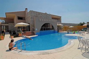 A swimming pool area with a stone building, lounge chairs, and umbrellas. - Astir Notos (Thasos)