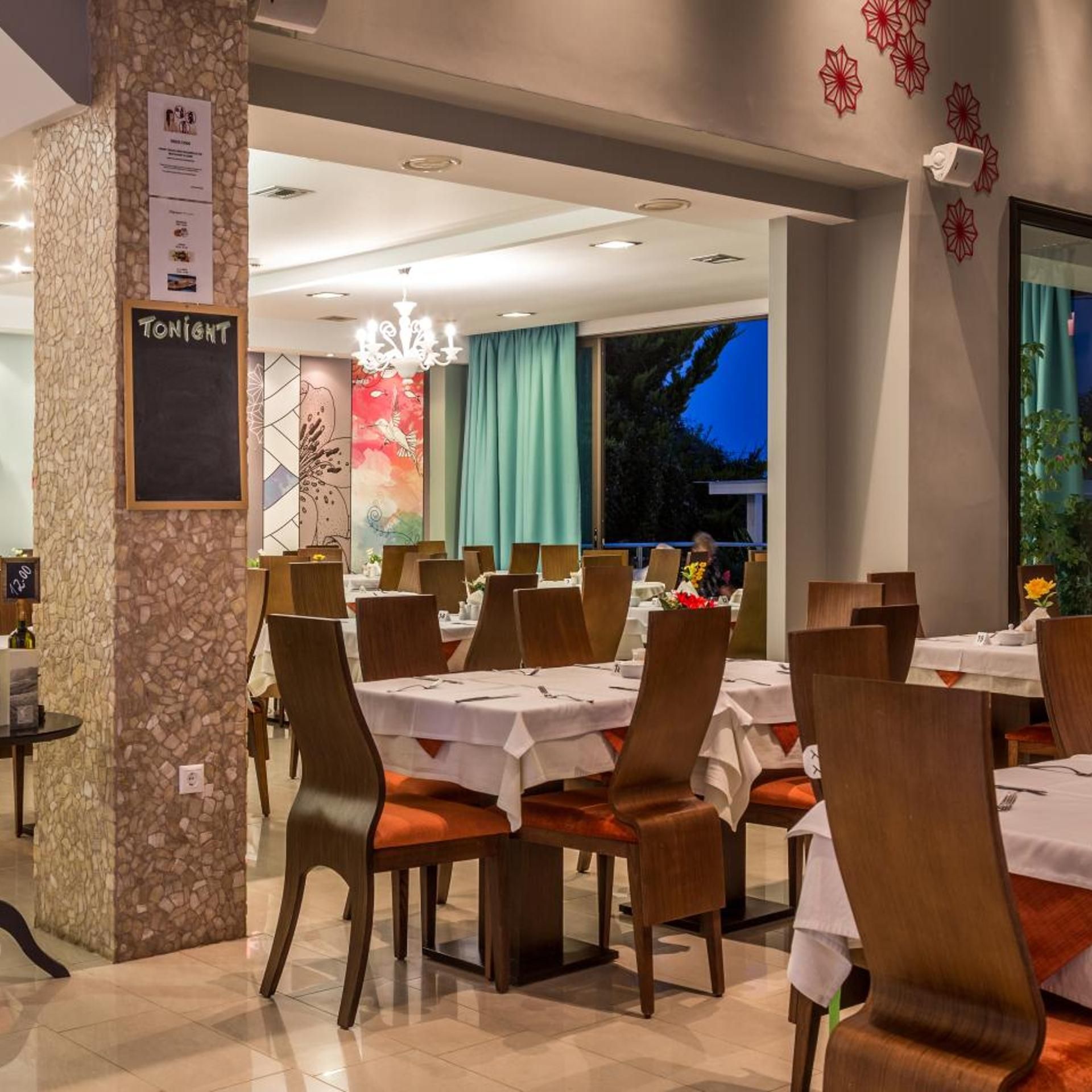 A restaurant with multiple tables and chairs, a stone pillar with a sign, and a view of the outdoors.