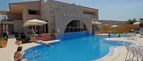 Un espace piscine avec un bâtiment en pierre, des chaises longues et des parasols.