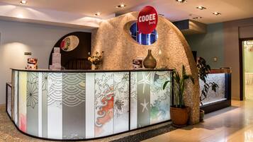 A reception desk with a stone facade, a 'COOEE' sign, and a large potted plant.