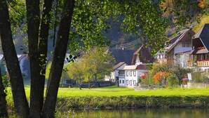Vista a la orilla del río con casas, árboles y una zona cubierta de césped.