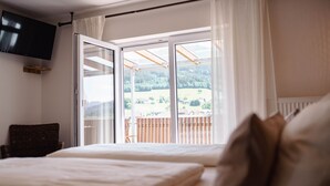 Un dormitorio con cama, televisor en la pared y vistas a un balcón con barandilla de madera.