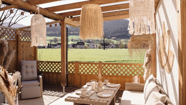 Una terraza de madera con una mesa dispuesta para comer, con vistas a un campo verde.