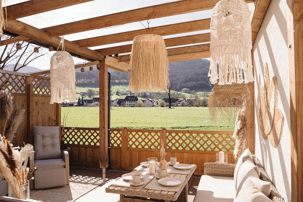 A wooden deck with a table set for dining, overlooking a green field.