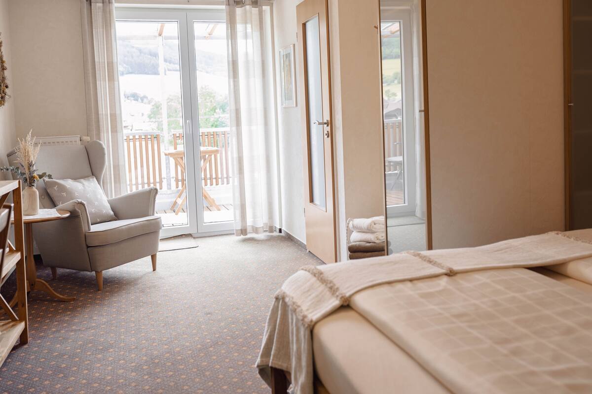 A bedroom with a bed, a chair, a desk, and a view of the outdoors.