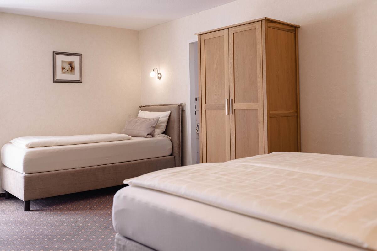 A bedroom with two beds, a wardrobe, a wall-mounted light, and a framed picture.